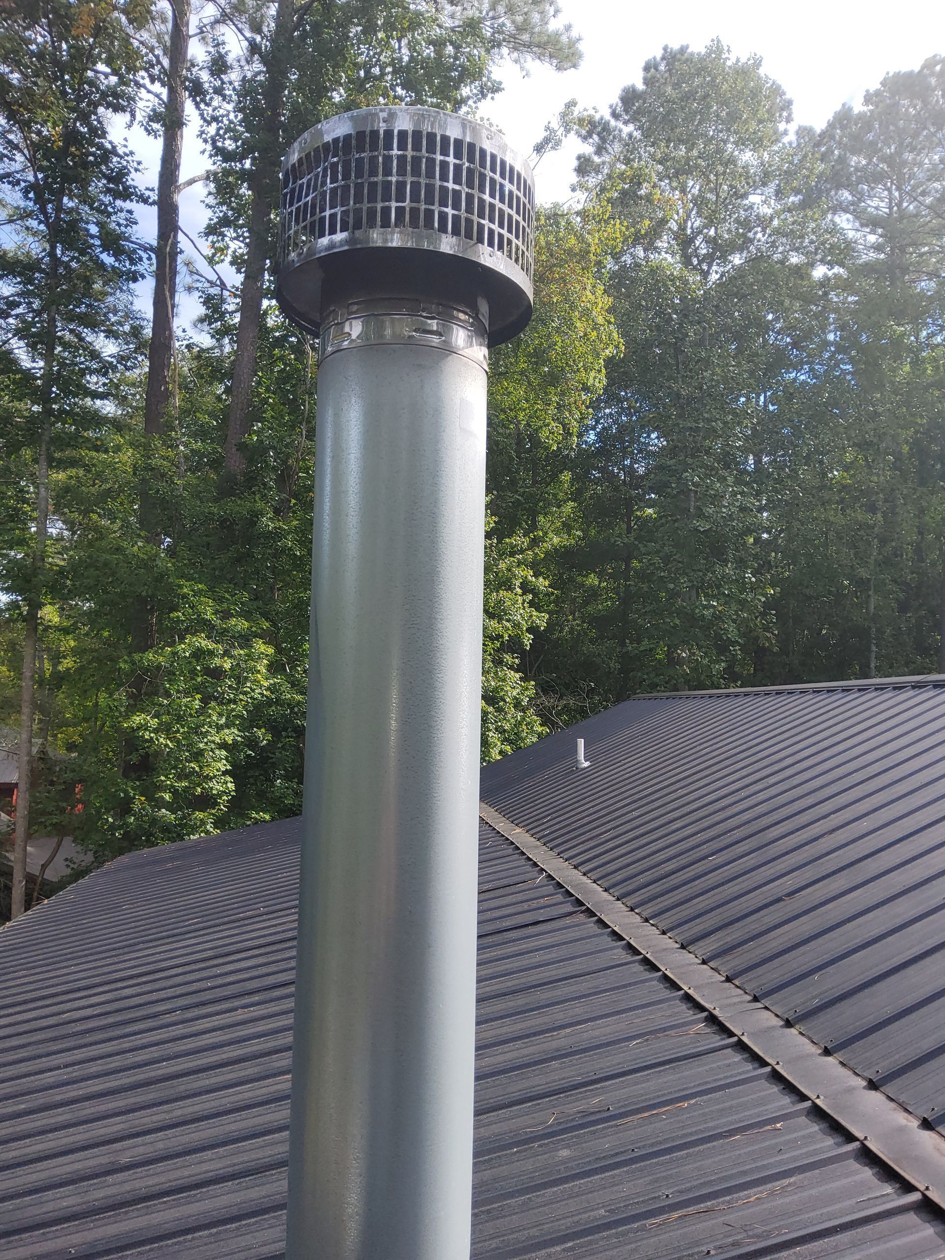 A chimney on top of a roof with trees in the background.