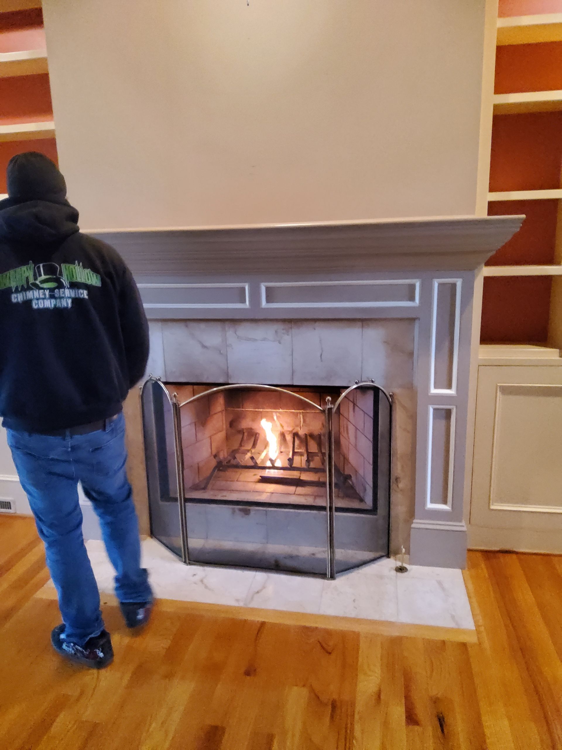 A man standing in front of a fireplace wearing a sweatshirt that says ' a ' on it