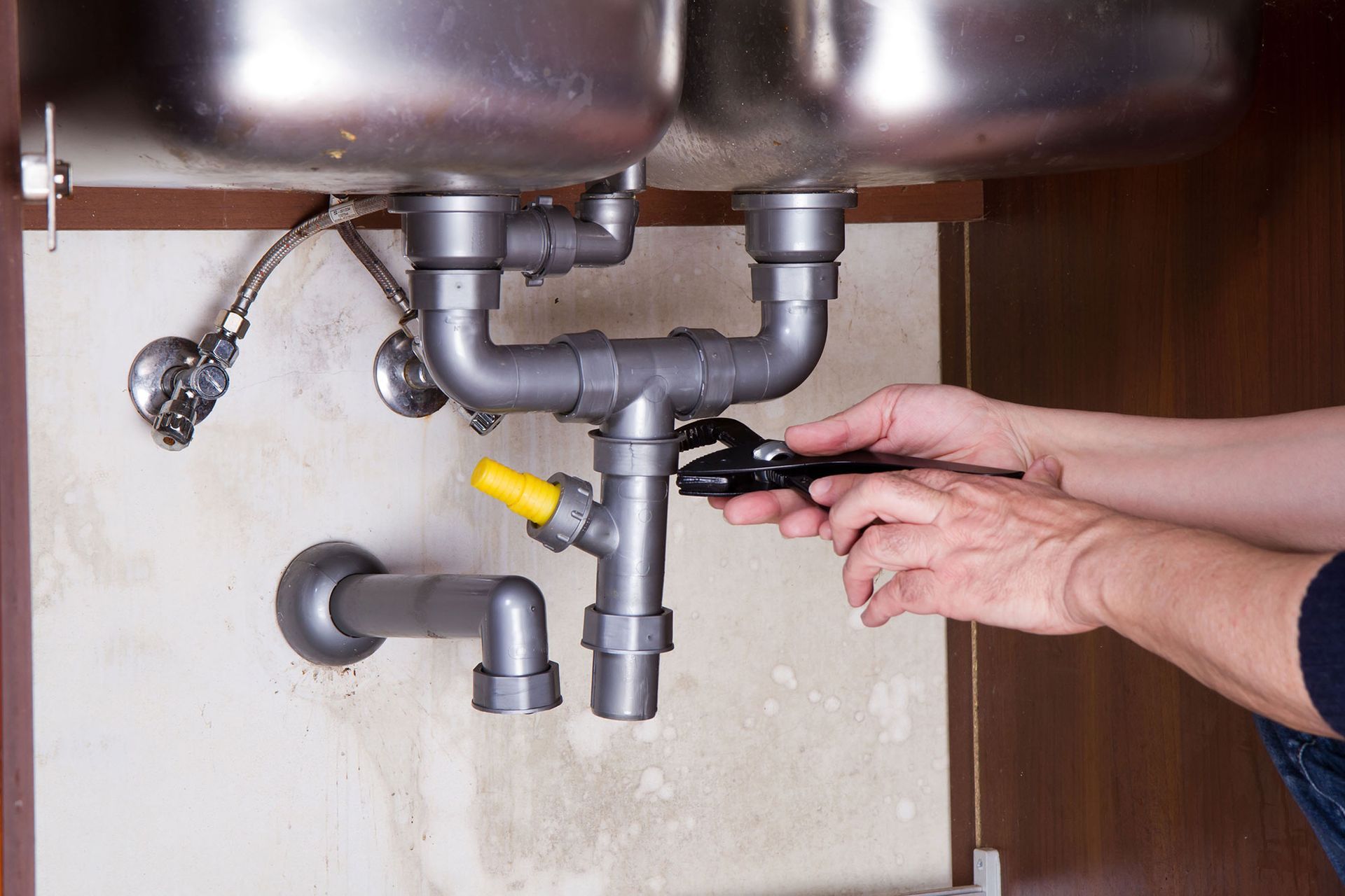A person is fixing a sink with a wrench.