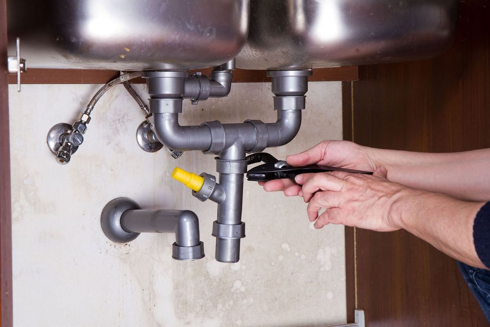 A person is fixing a sink with a wrench.