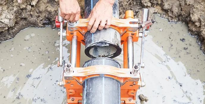 A man is working on a pipe in the dirt with a machine.
