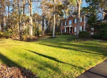 A two-story brick house with a green lawn surrounded by trees.