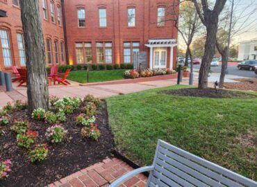Red brick building with landscaped yard, flowers, trees, and bench.