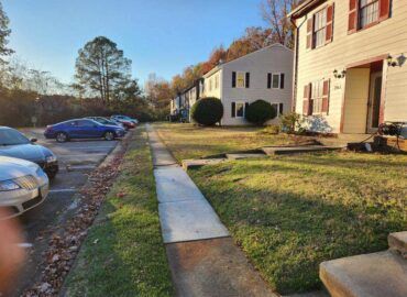 Apartment buildings with parked cars and a walkway on a sunny day.