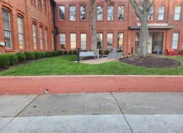 Red brick building with windows, a small lawn, and a sidewalk; the building entrance has a sign that reads 