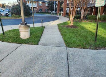 Concrete sidewalk curves through grass toward a building entrance.