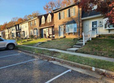 Row of townhouses with varying colored siding, short grass lawns, and parked car.