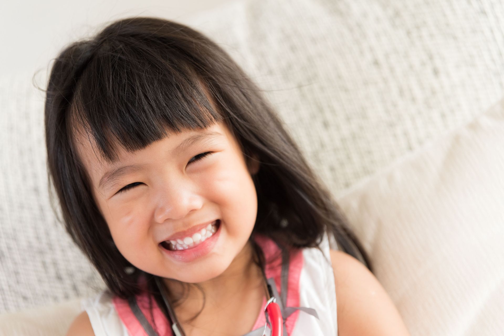 Smiling child with long dark hair, wearing a white and pink top.