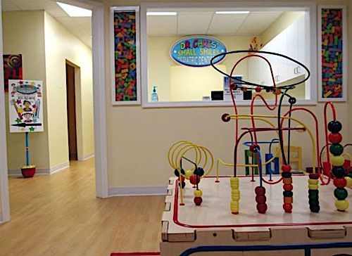 Play area in a children's medical office with colorful toys, a hallway, and a reception window.
