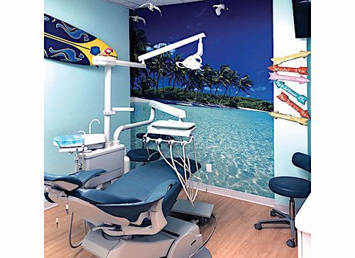 Dental office with a blue chair, beach mural, and surfboard decor.