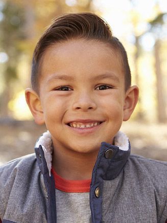 Smiling child in gray vest, outdoors.