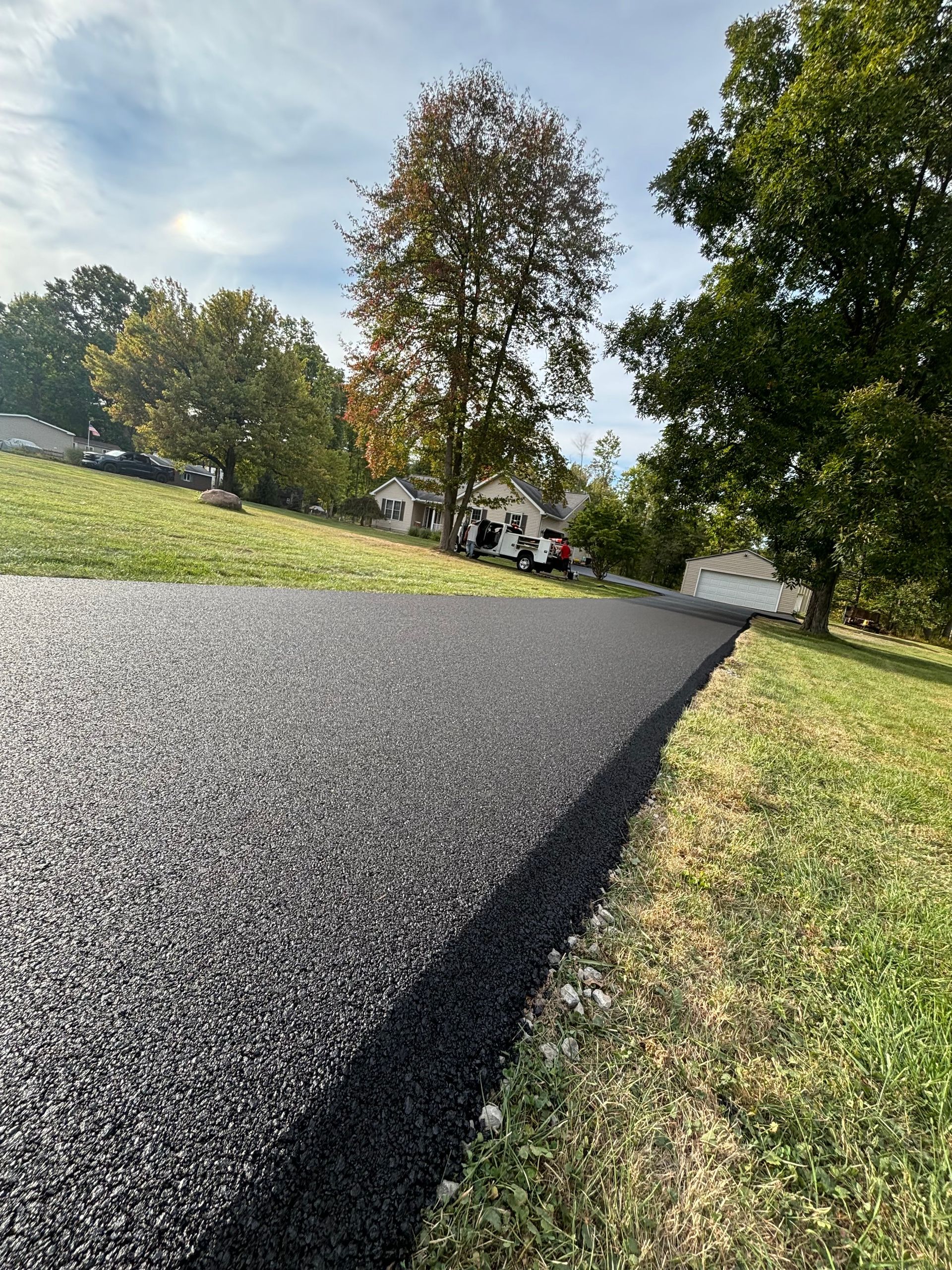A black asphalt driveway surrounded by grass and trees.