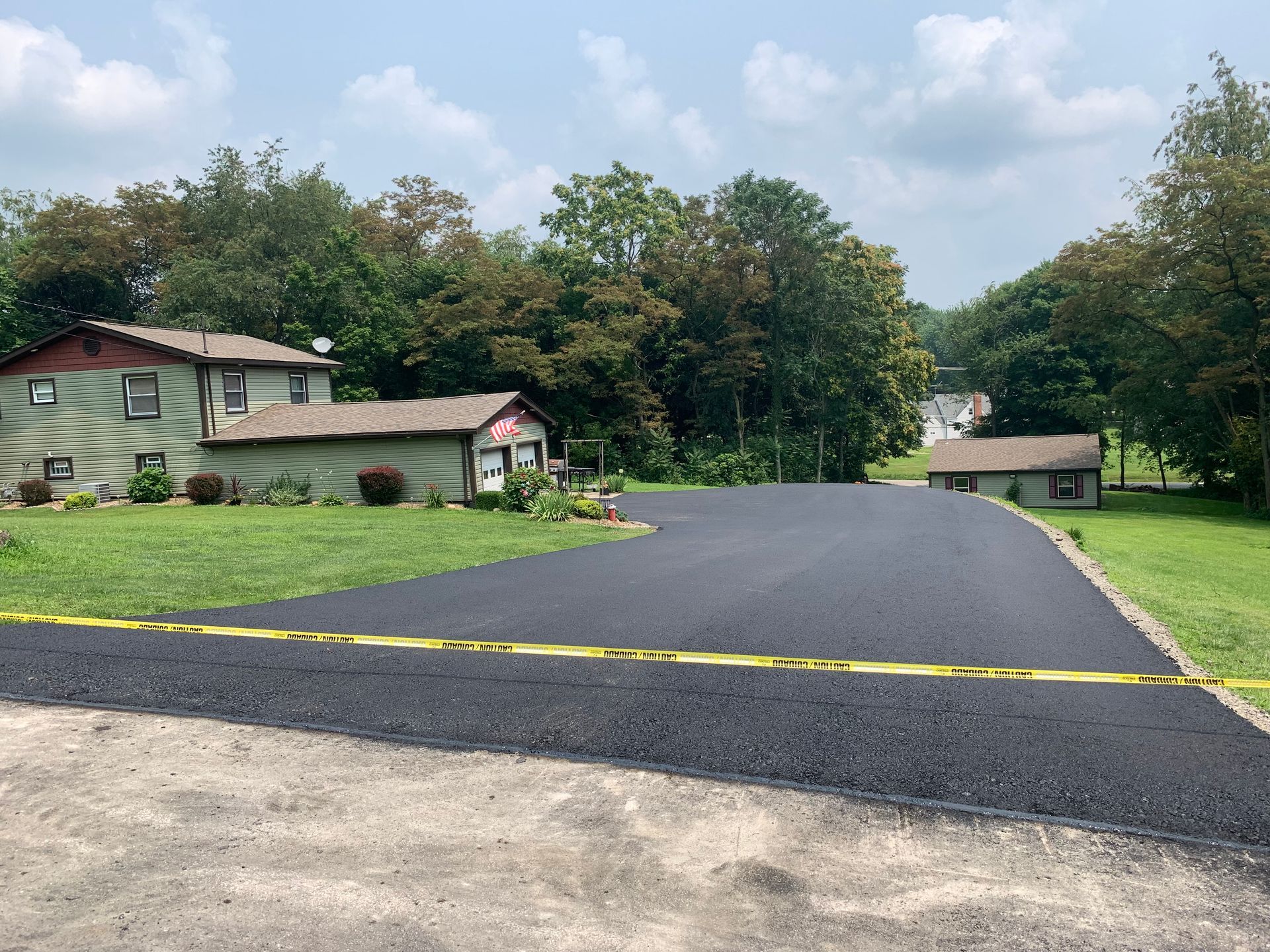 A road with a yellow tape along the side of it and a house in the background.
