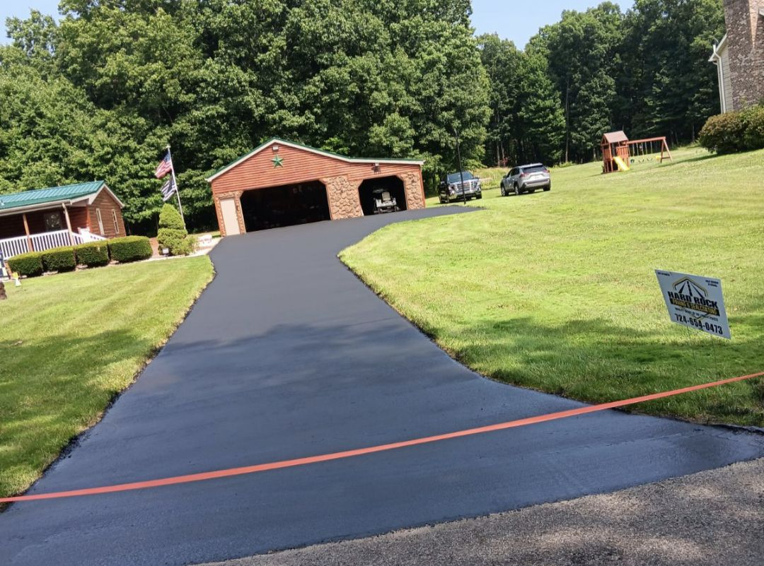 A driveway leading to a house with a garage and a sign in the grass.