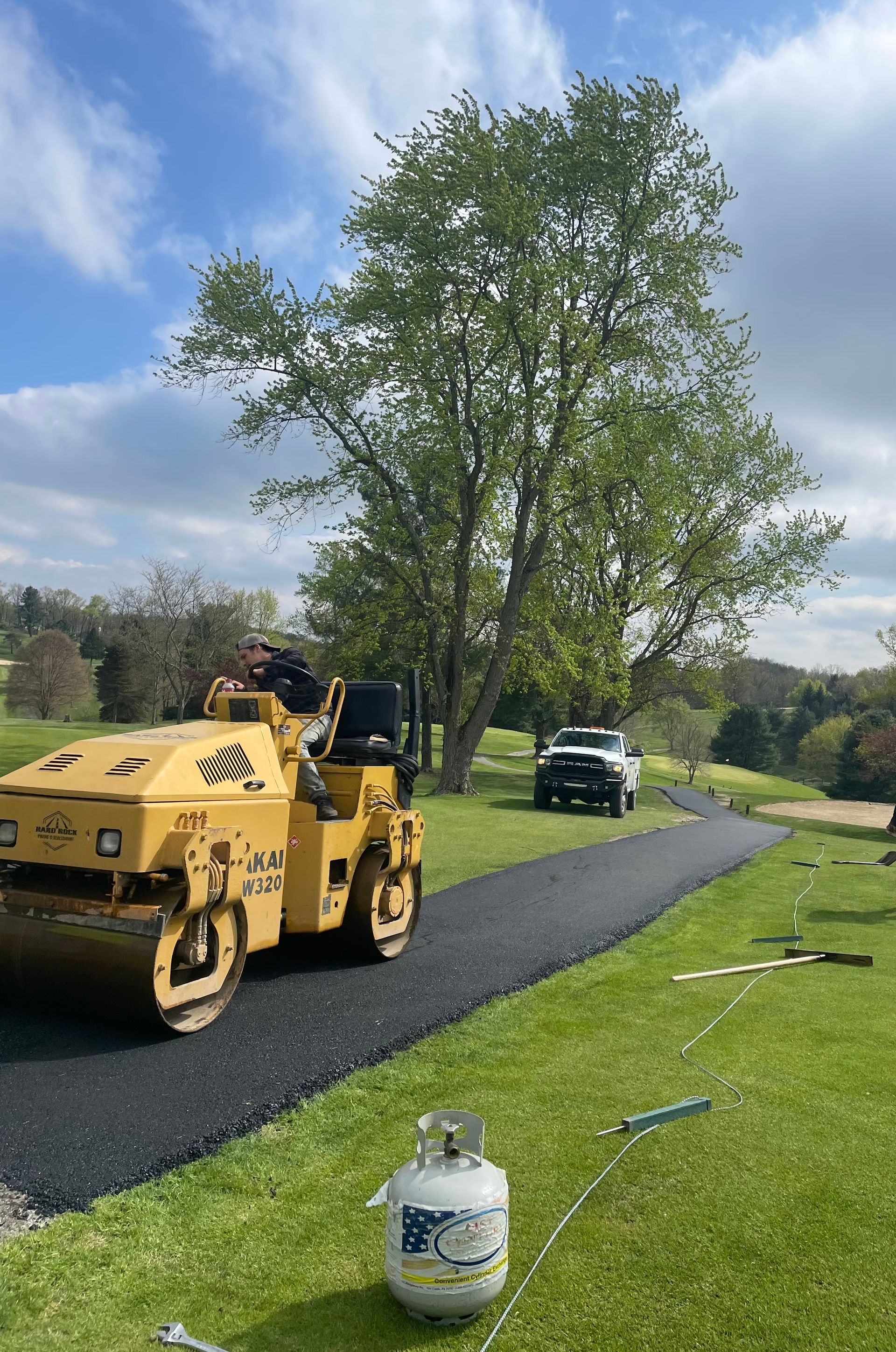 A yellow roller is laying asphalt on a golf course.