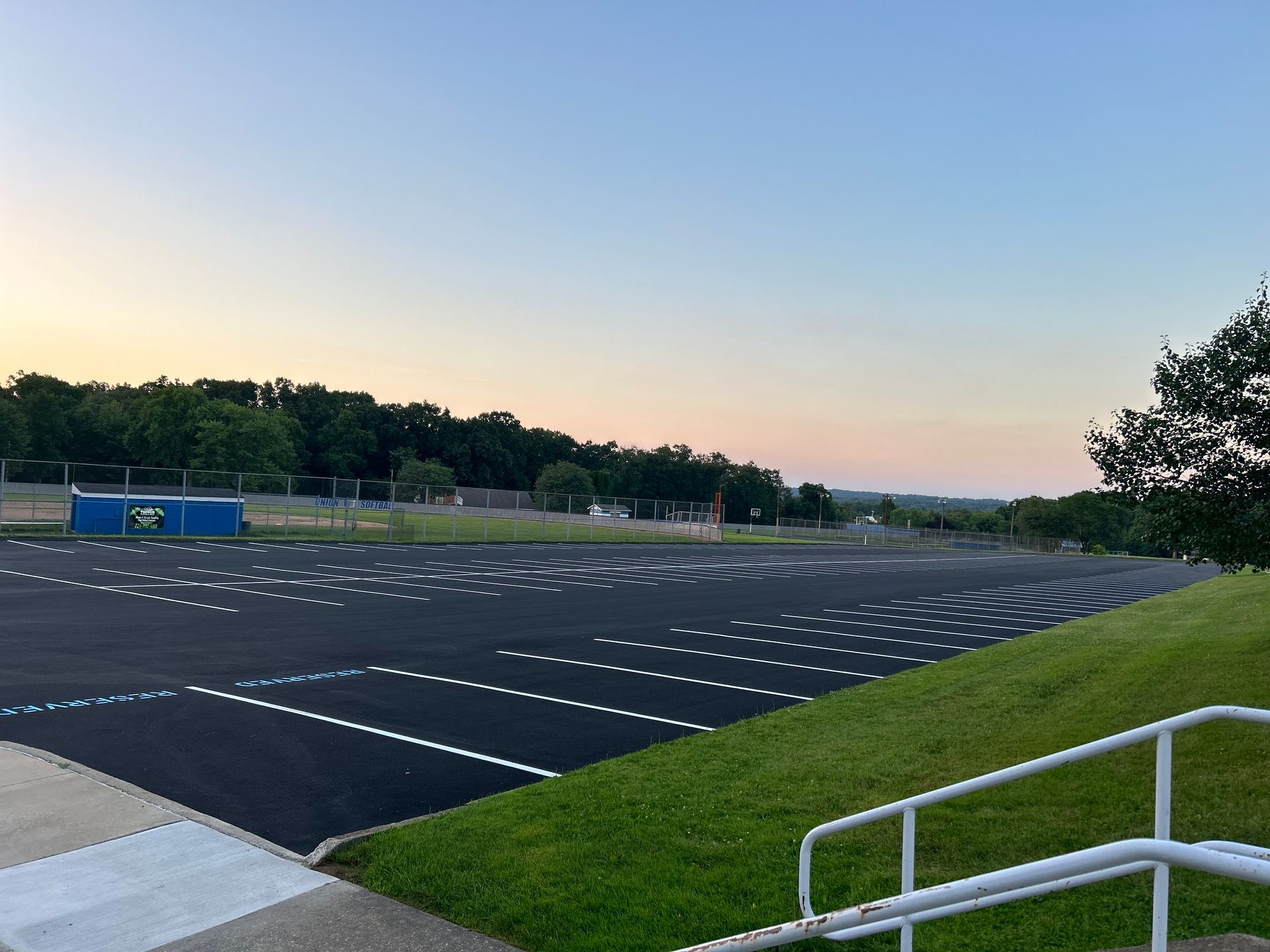 A parking lot with a fence and stairs in the foreground and trees in the background.