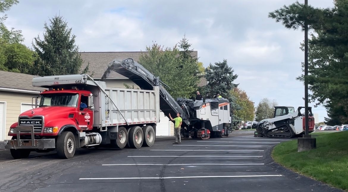 A dump truck is being loaded with asphalt in a parking lot.