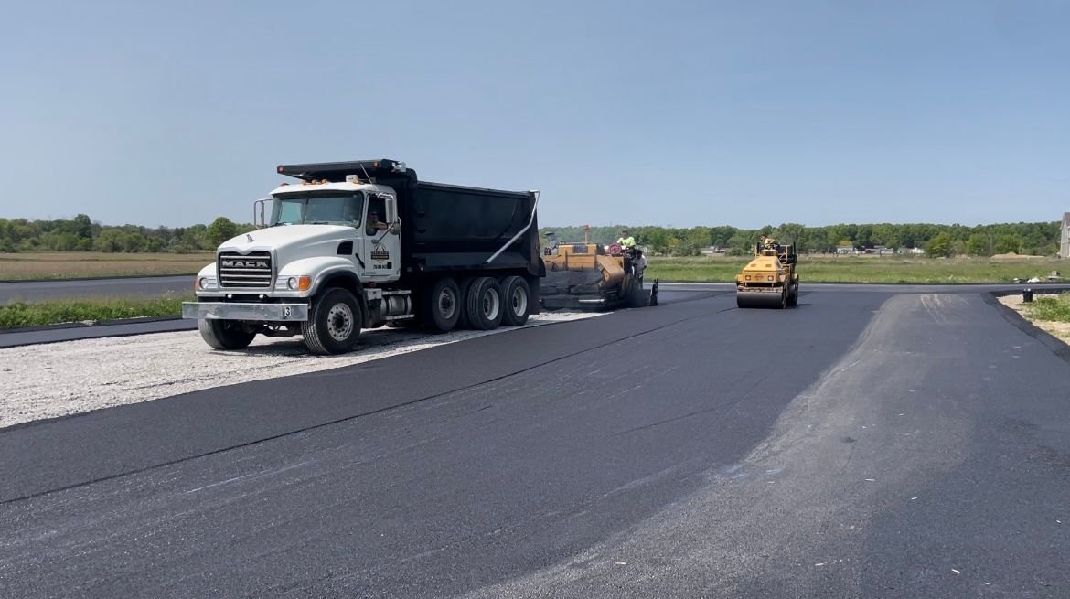 A dump truck is driving down a road next to a roller.