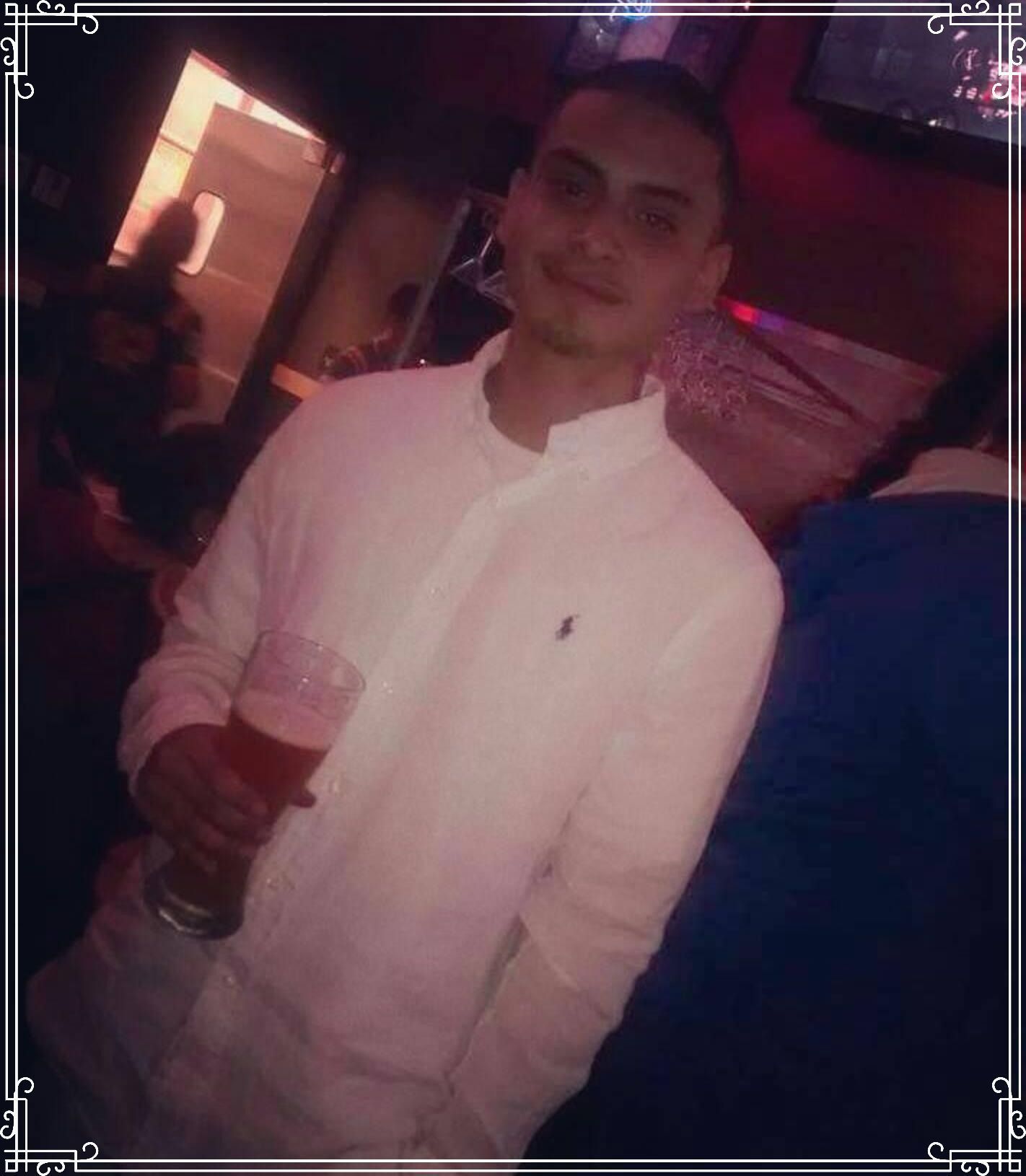 Person in a white shirt holding a drink at a dimly lit indoor party.