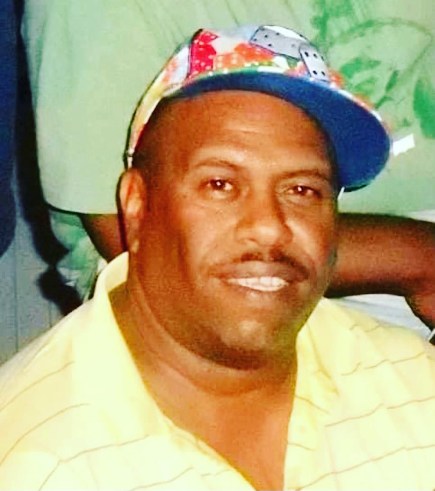 Man in a yellow shirt and colorful cap, smiling in a close-up portrait.