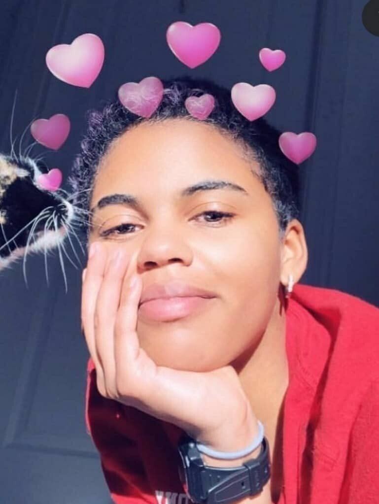 Person resting their face on their hand, wearing a red top, with pink heart stickers above their head.