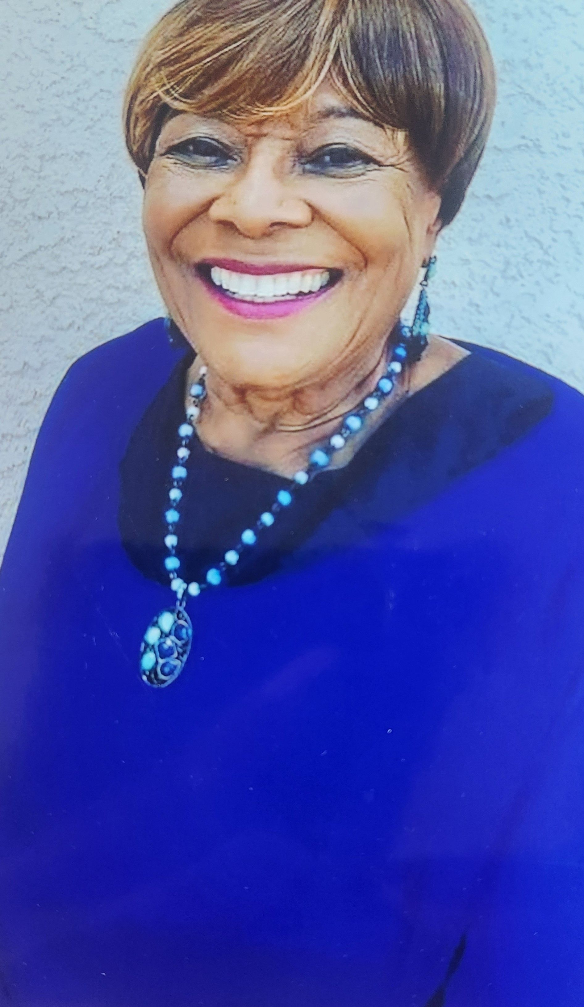 Smiling person in a bright blue top and matching necklace, posed against a light background.