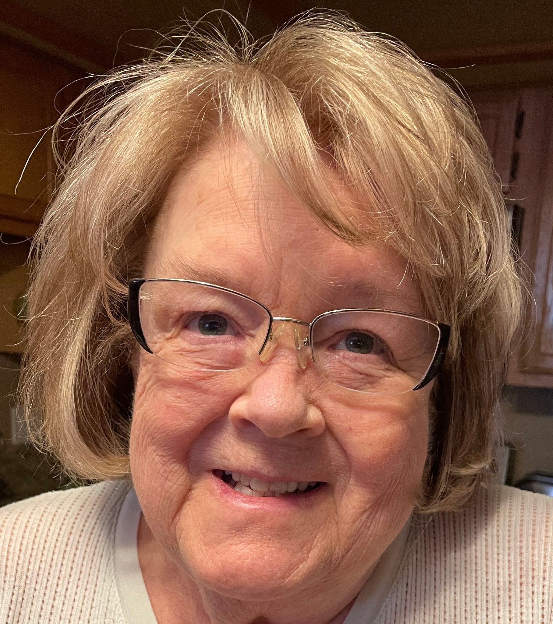 Smiling woman with glasses in a cozy indoor setting, wearing a light sweater.