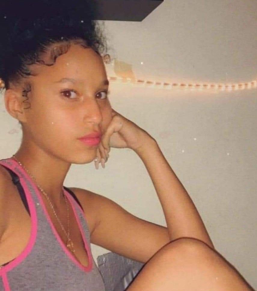 Person sitting indoors, resting their head on one hand, wearing a black tank top with pink trim.