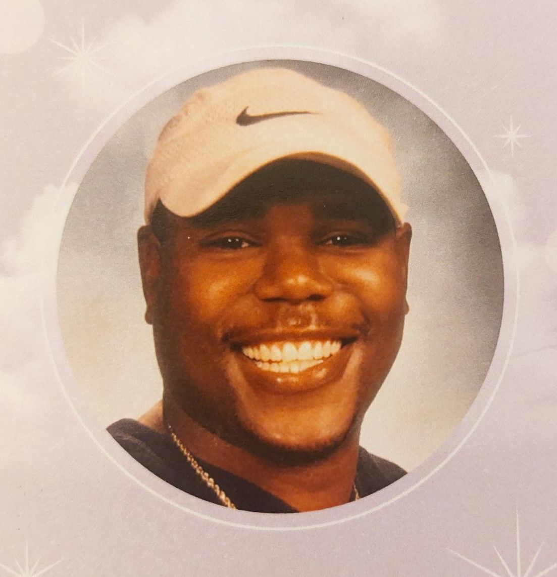 Smiling man in a white Nike cap against a soft pink, sparkly background