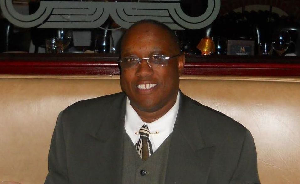 Smiling man in glasses and a suit sitting in a restaurant booth.