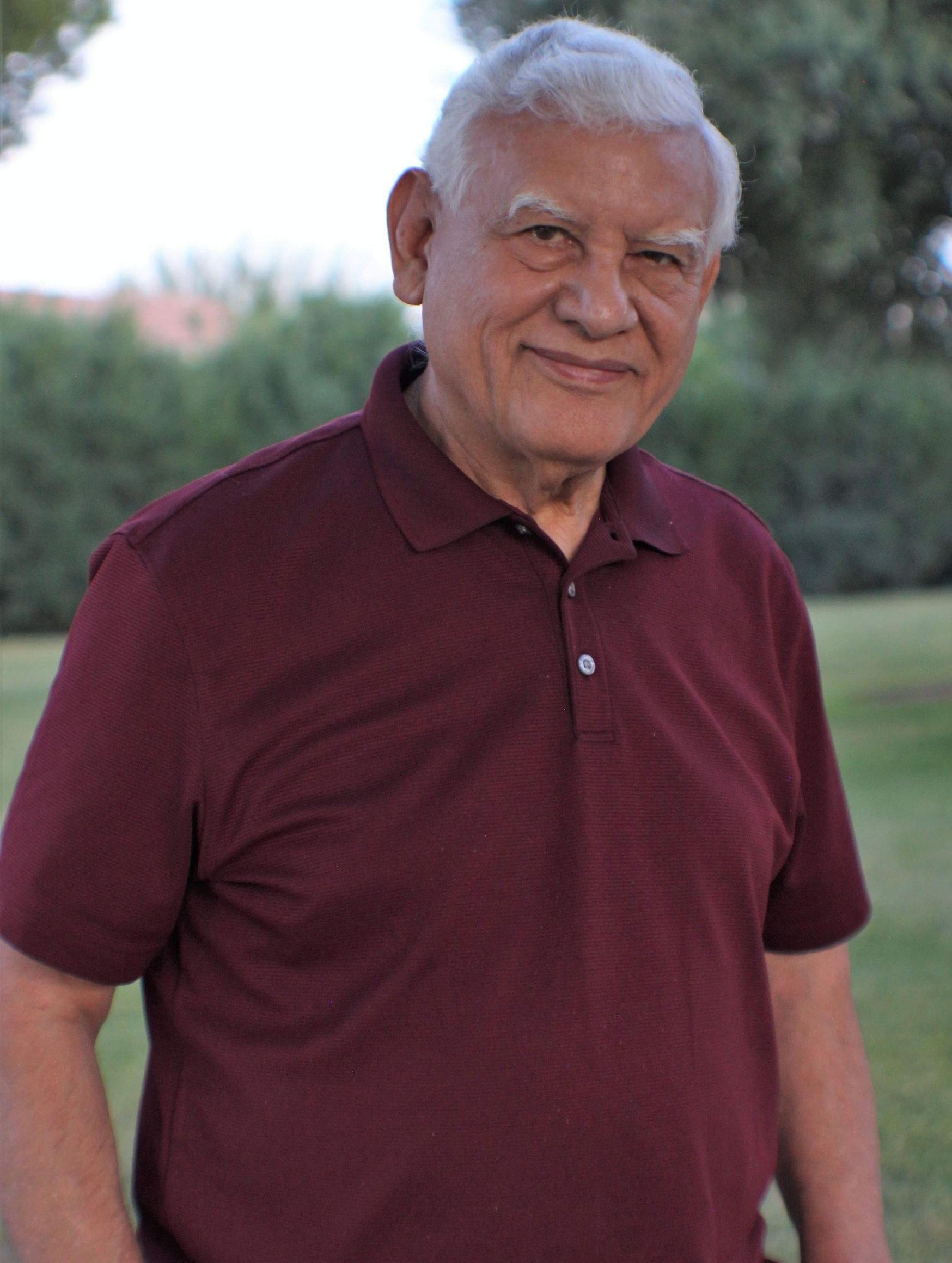 Smiling man in a maroon polo shirt standing outdoors with a blurred green background