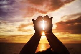 Silhouette of raised hands framing a glowing cross at sunset over a beach