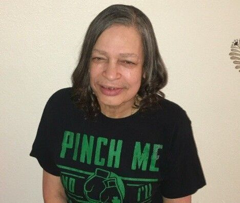 Person smiling in a black “PINCH ME” T-shirt against a plain wall.