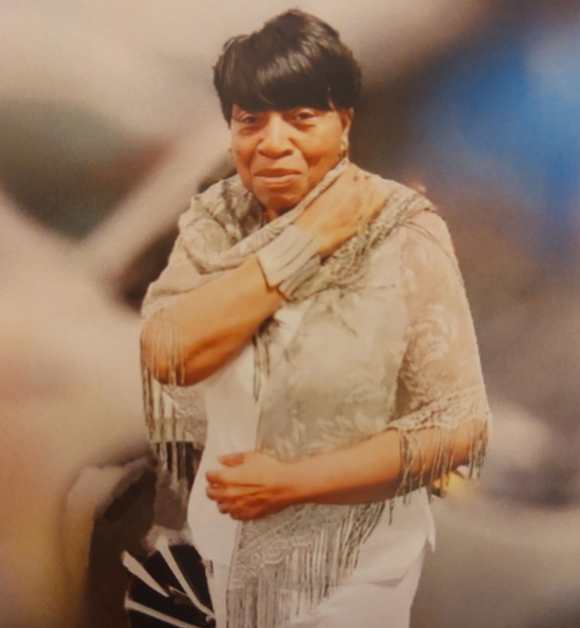 Person in a white outfit adjusting a beige scarf, standing against a blurred background.