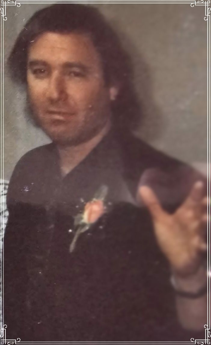 Portrait of a man in a dark suit, facing forward with one hand raised, against a plain background