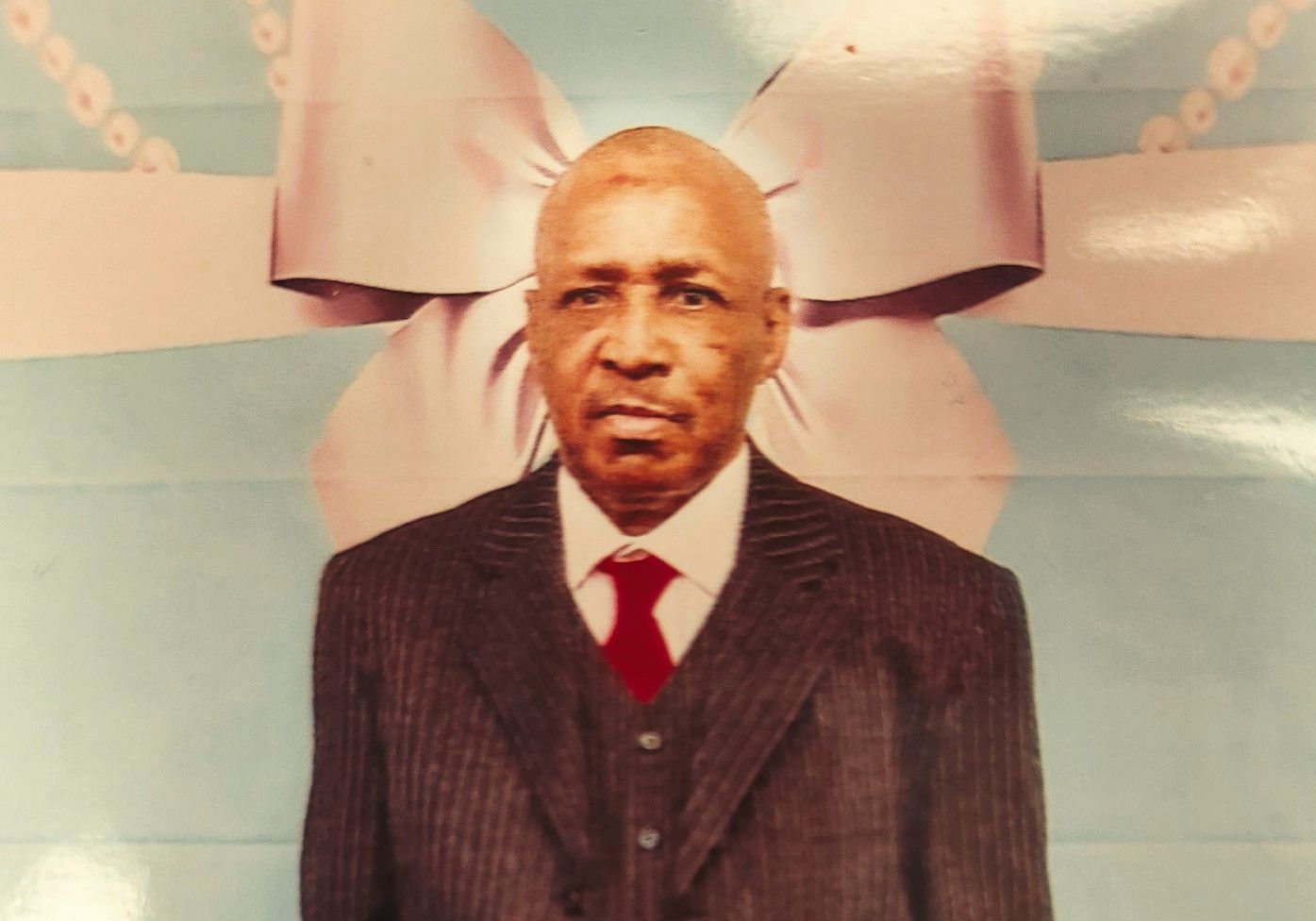 Portrait of a man in a dark suit and red tie standing before a pastel backdrop