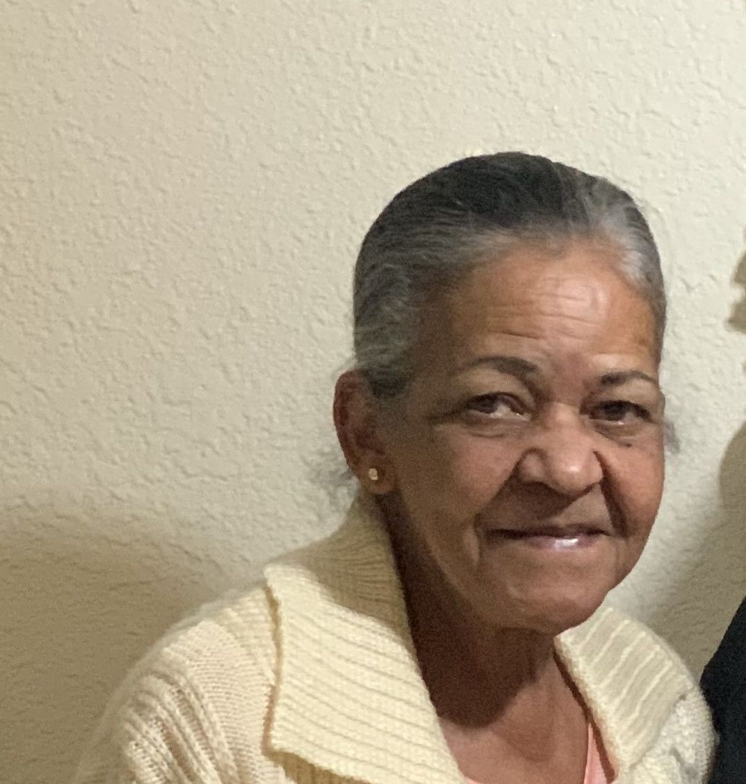 Smiling woman in a cream sweater against a beige wall.