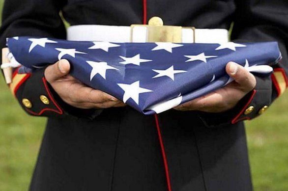 Hands holding a folded American flag with a white cross on a dark uniform