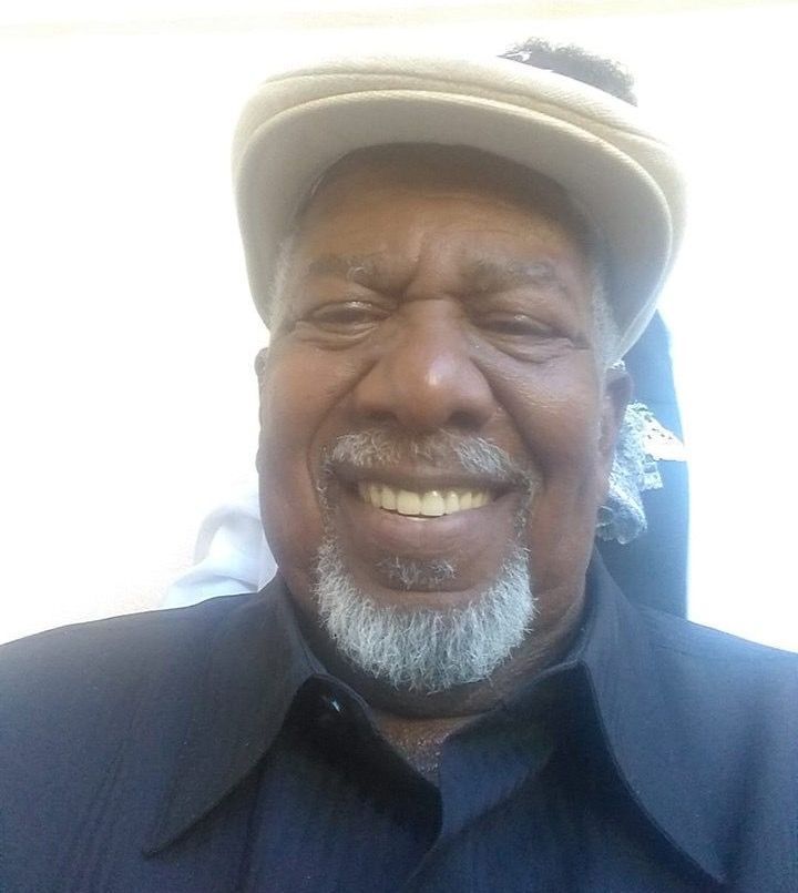 Smiling man in a light cap and dark shirt, close-up portrait against a bright background