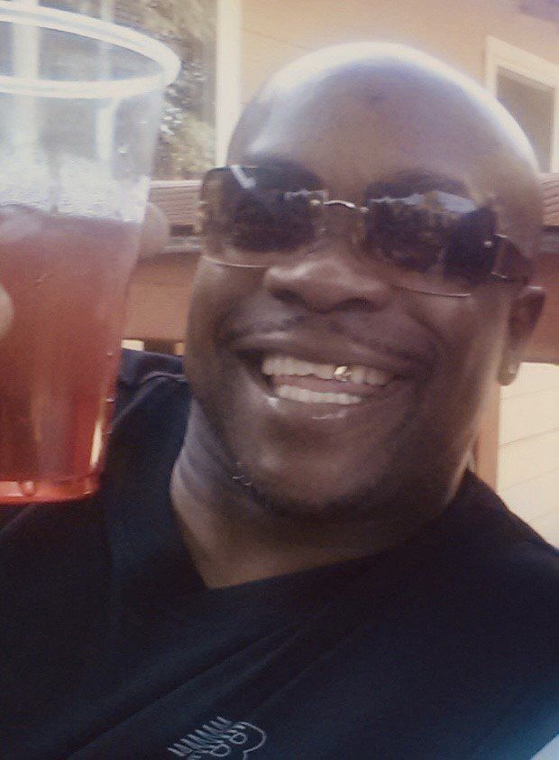 Smiling man in sunglasses holding a drink in a clear plastic cup outdoors