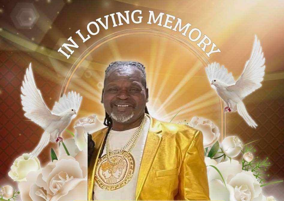 Memorial tribute with smiling man in gold attire, white doves, flowers, and “In Loving Memory” text