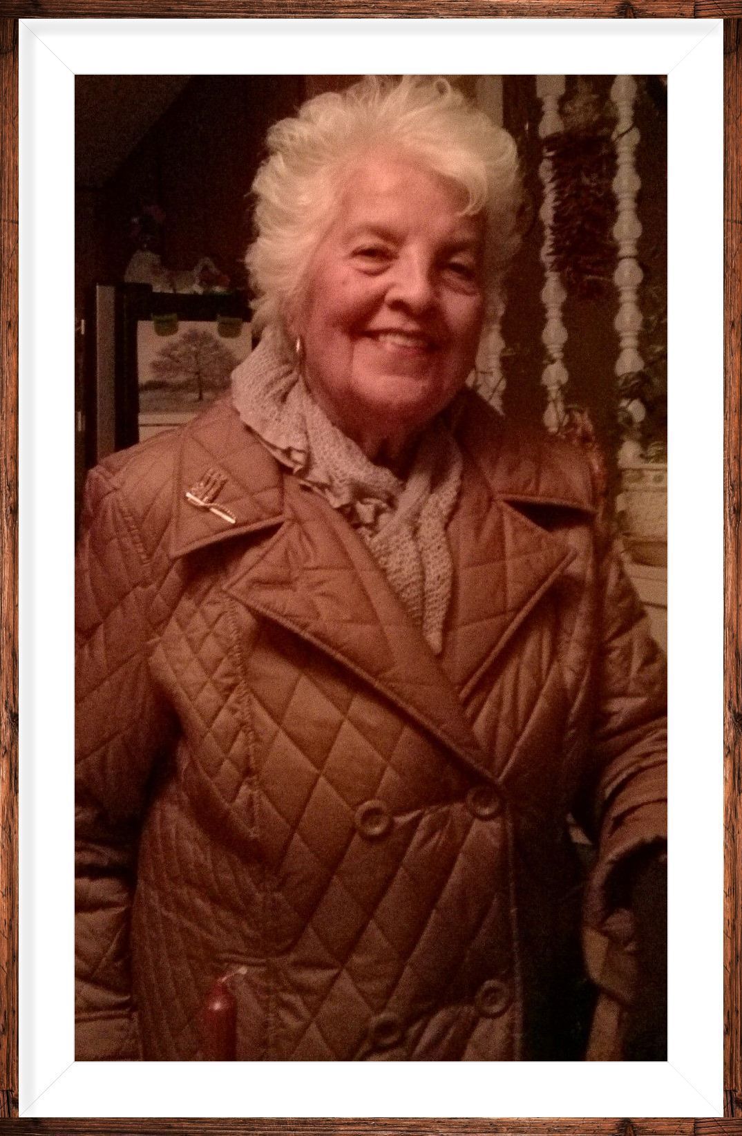 Portrait of a smiling person in a tan quilted coat indoors, framed in white