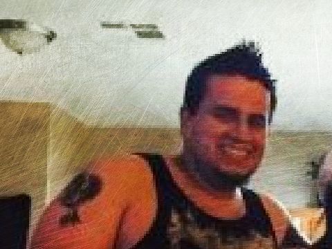 Smiling person in a black tank top with a tattoo, indoors under bright ceiling lights