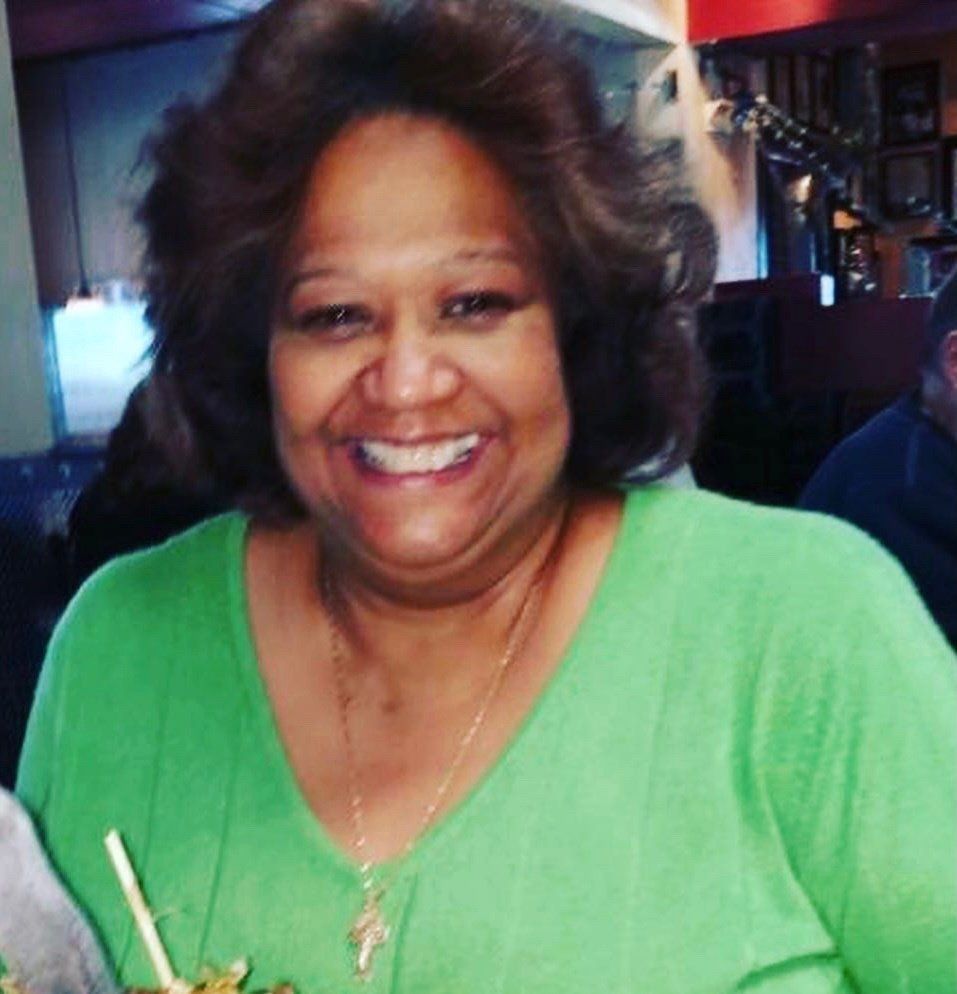 Smiling person in a bright green top at a restaurant table, holding chopsticks