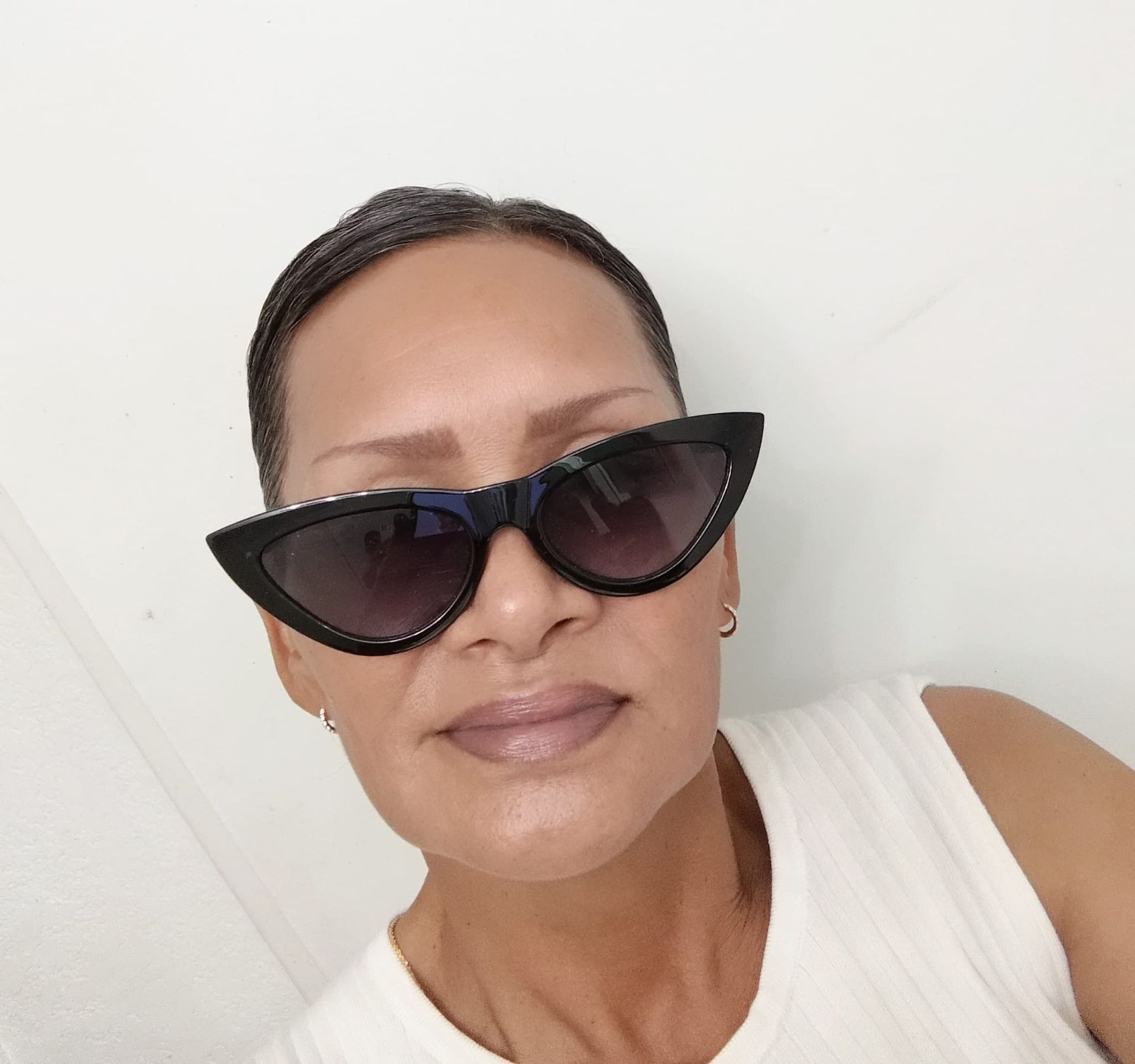 Person in black cat-eye sunglasses and white top against a plain white background.