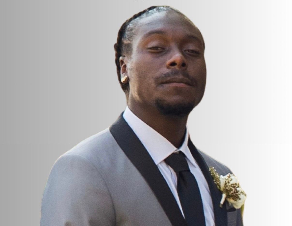 Portrait of a man in a gray suit and black tie, standing against a light background