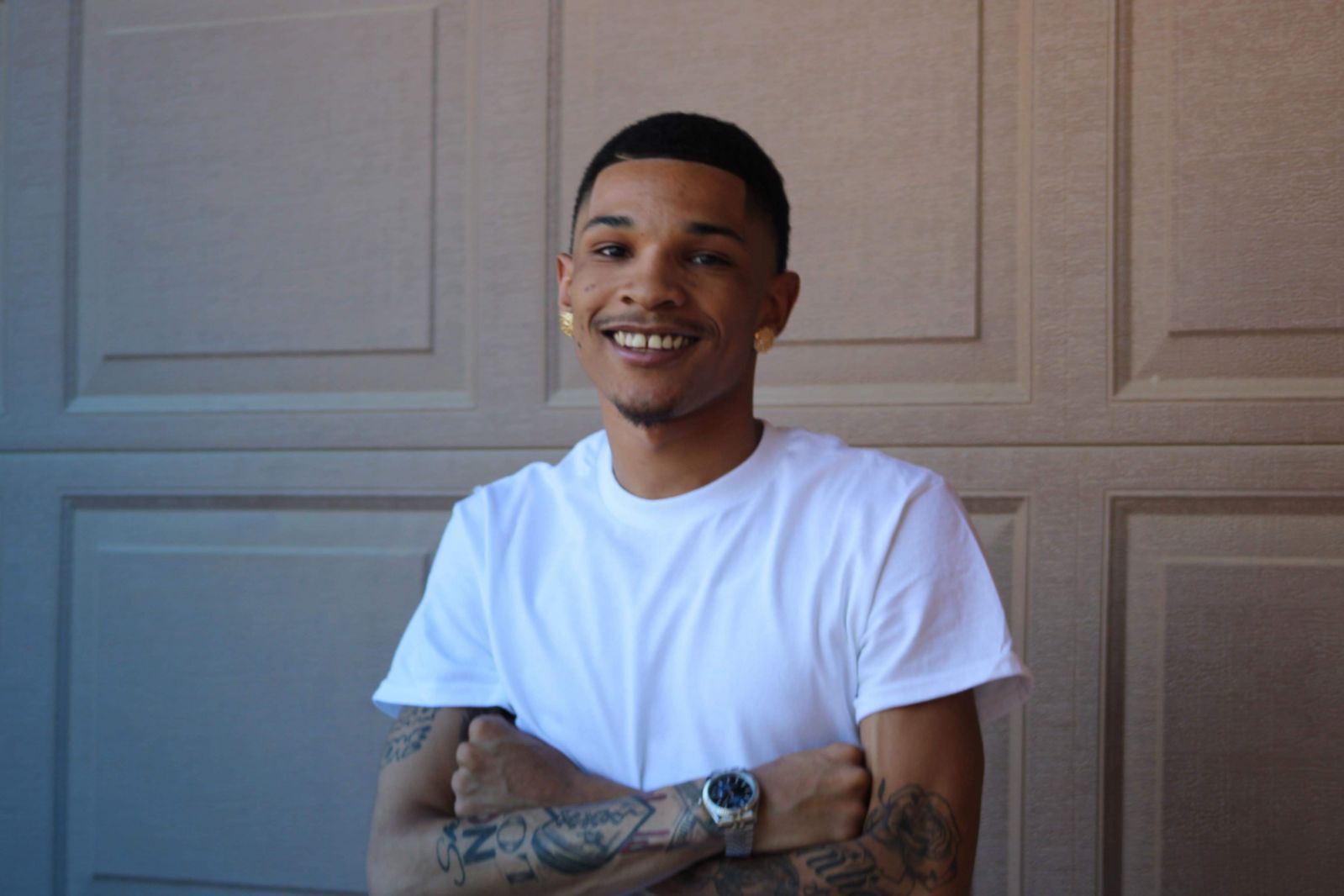 Smiling person in a white T-shirt with crossed arms, standing in front of beige garage doors