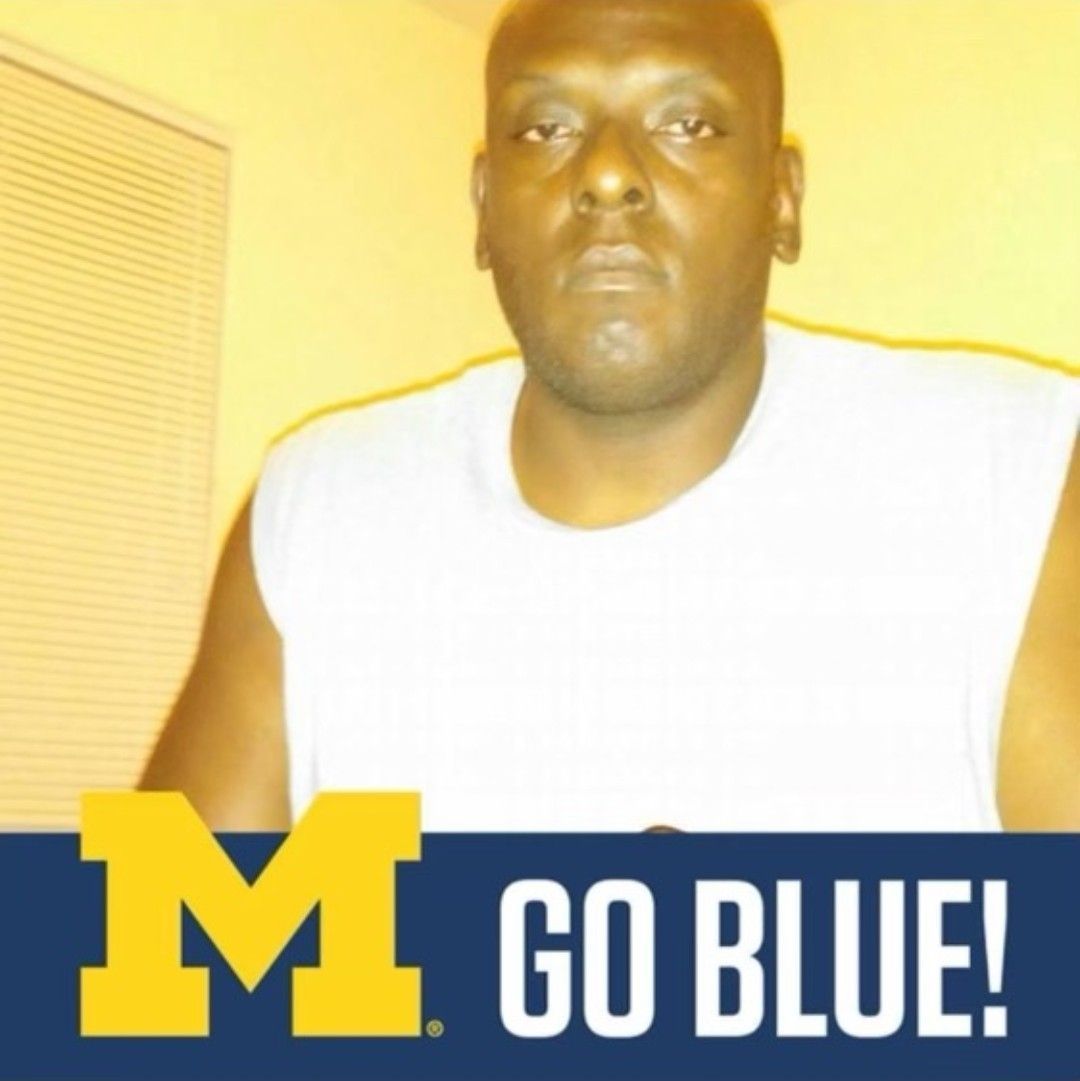 Person in a white sleeveless shirt posing with a Michigan Wolverines logo and “GO BLUE!” text.
