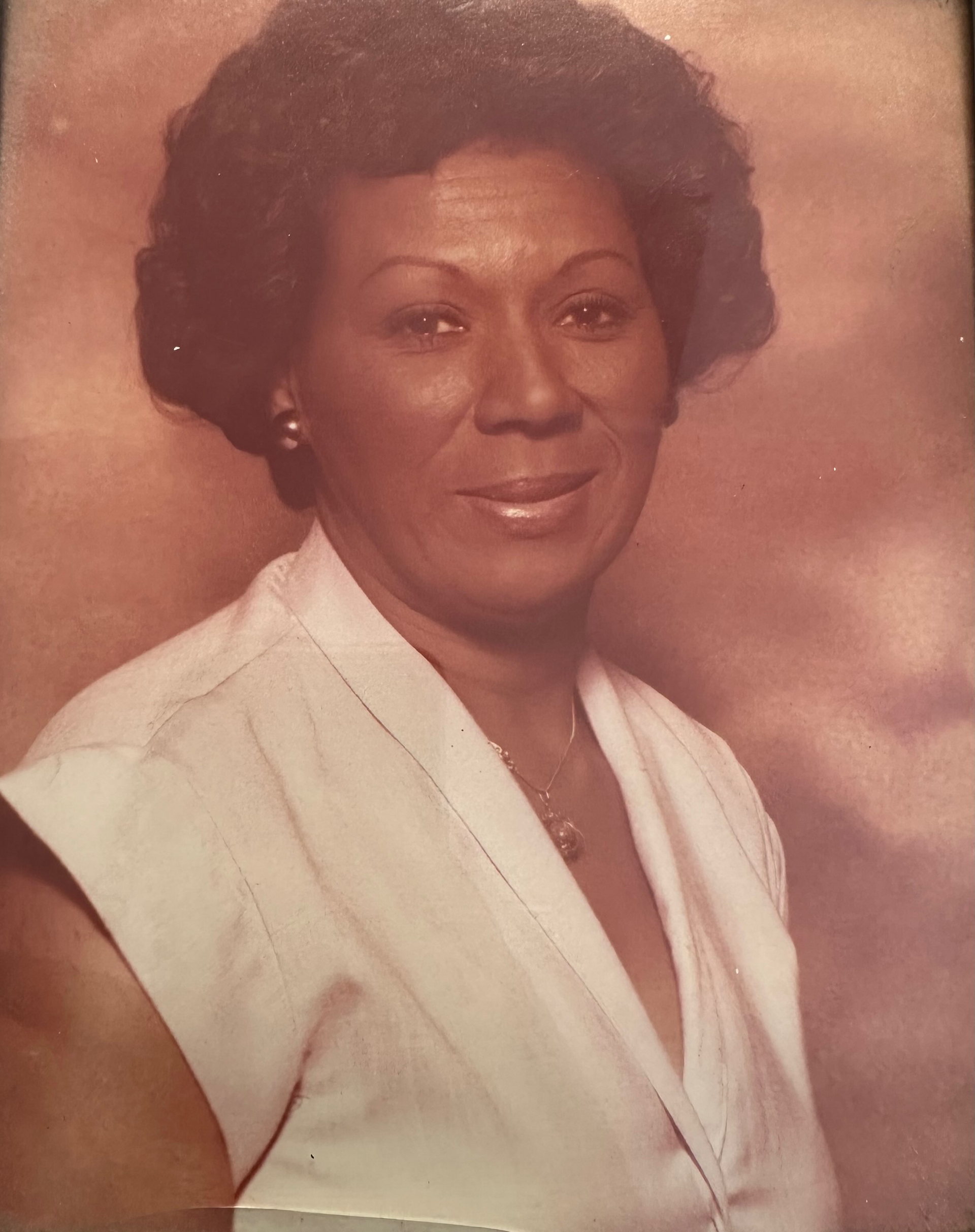 Studio portrait of a woman in a light blouse, smiling against a soft pink background