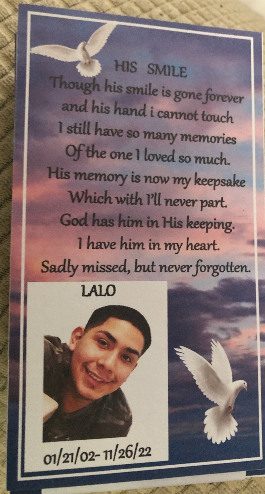 Memorial poster with poem, doves, and a smiling portrait of Lalo on a blue cloudy background